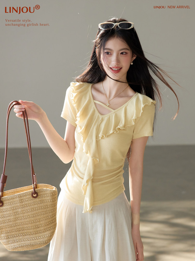 Model wearing a light yellow ruffled top and holding a straw tote bag