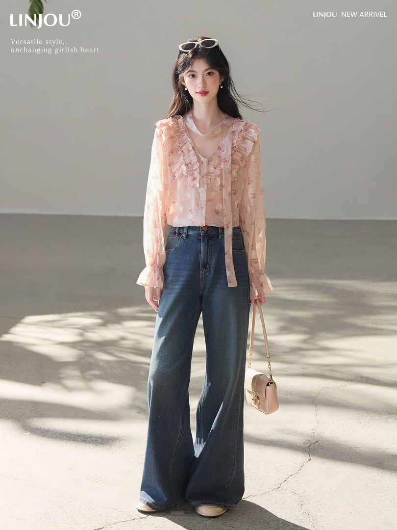 Model wearing a pink ruffled floral blouse with wide-leg jeans and a small handbag