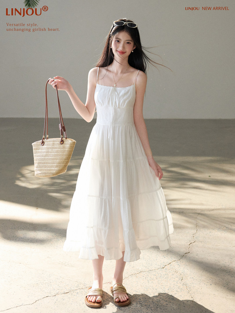 Woman wearing a white spaghetti-strap midi dress and holding a straw tote bag