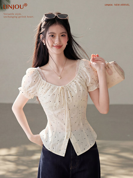 Model wearing a white polka dot puff-sleeve blouse with a small handbag