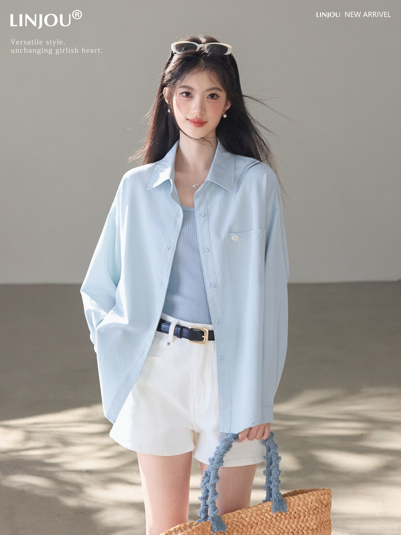 Model wearing a light blue oversized button-down shirt with white shorts and a straw tote bag