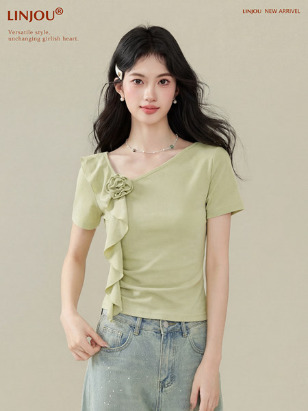 Model wearing a light green short-sleeve top with ruffle floral detail and jeans