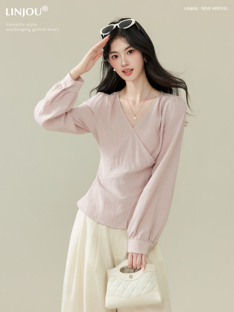 Model wearing a light pink wrap blouse with a cream skirt and white handbag in a studio fashion shot