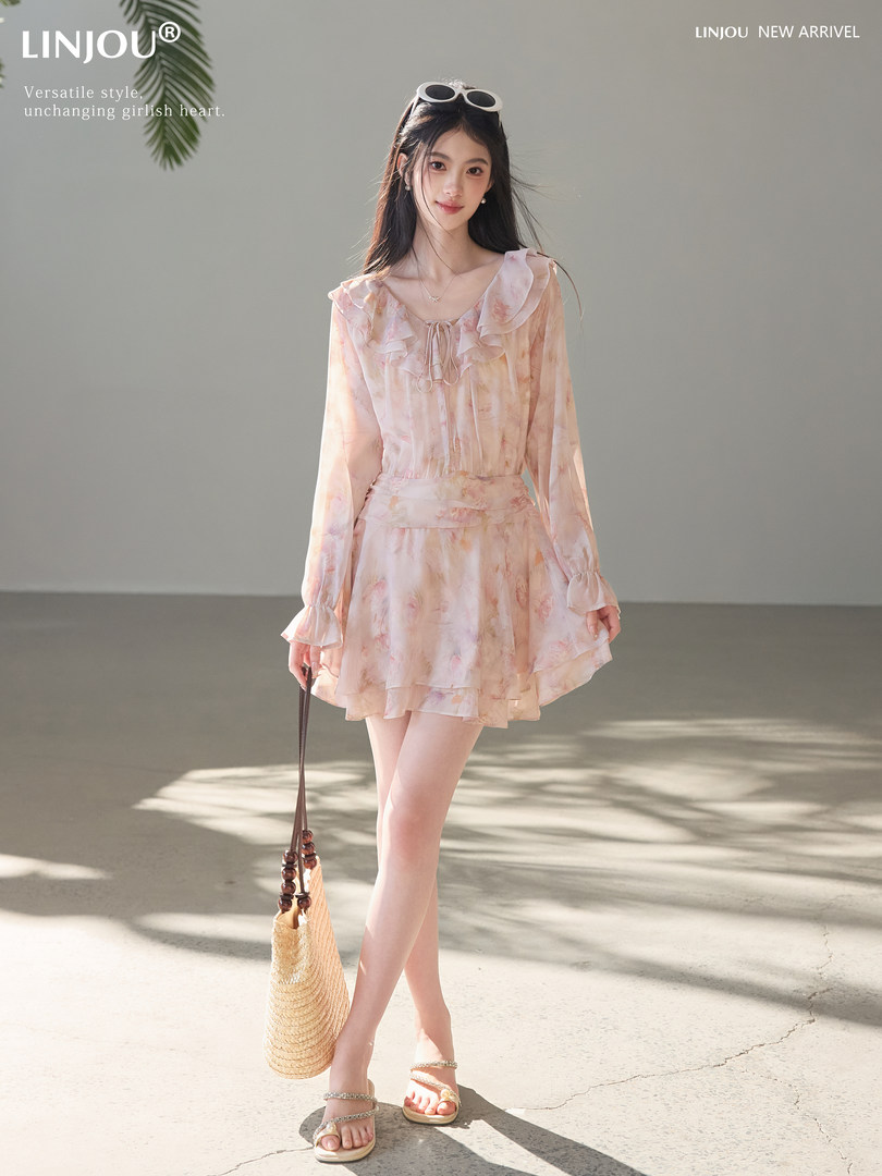 Model wearing a light pink floral ruffle dress with a woven straw bag and sandals