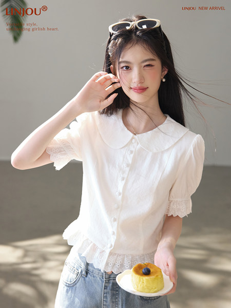 Model wearing a white short-sleeve blouse with lace trim and a Peter Pan collar