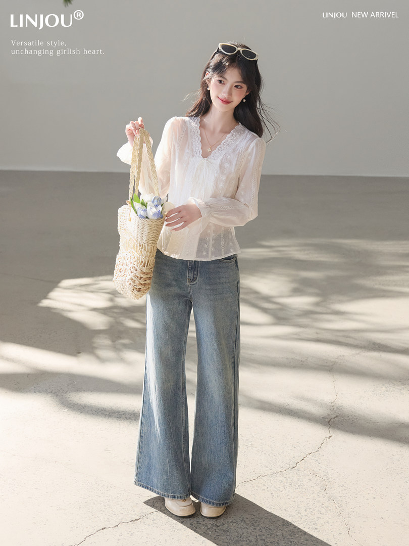 Model wearing a white lace blouse with wide-leg blue jeans and a woven tote bag