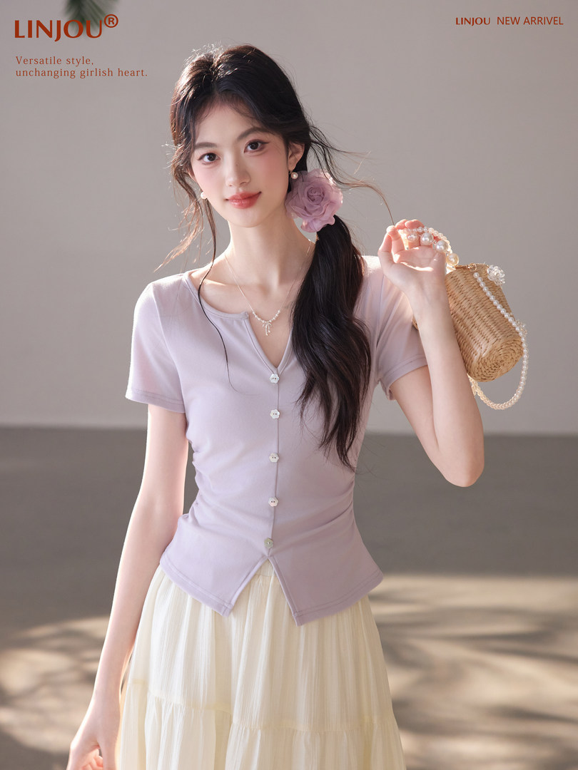 Woman wearing a light lavender button-front short-sleeve top with a cream skirt and handbag