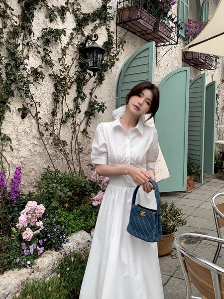 Woman wearing a white collared dress and holding a blue handbag