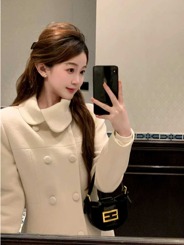 Woman wearing a cream double-breasted coat with a black handbag