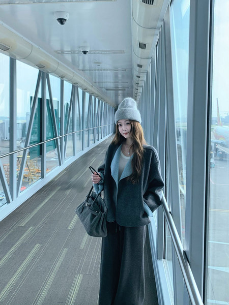 Woman wearing a dark oversized coat and knit beanie while carrying a handbag in a glass walkway
