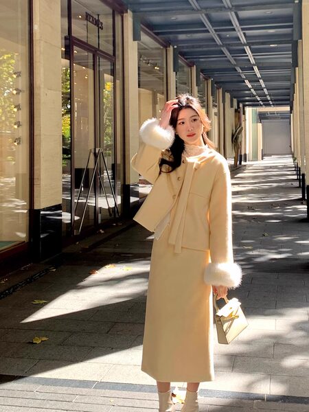 Woman wearing a cream coat and matching skirt set with fur-trim accents