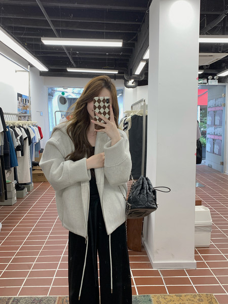 Mirror selfie of a woman wearing a light gray zip-up jacket with black wide-leg pants in a clothing store