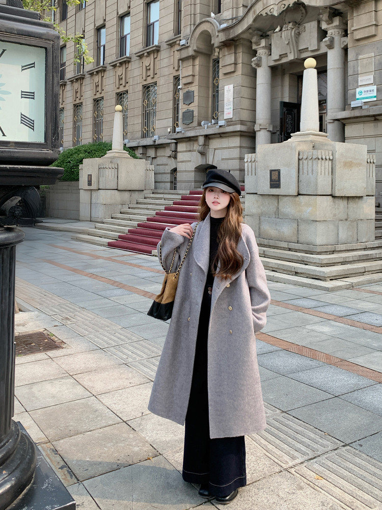 Woman wearing a long gray coat with a black hat and shoulder bag outdoors