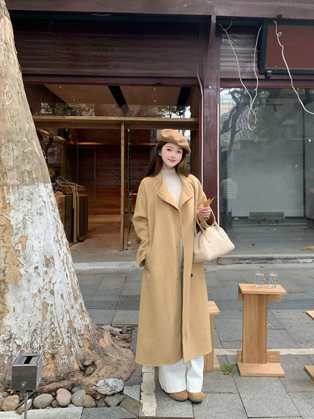 Woman wearing a long camel coat with a beret and handbag outdoors