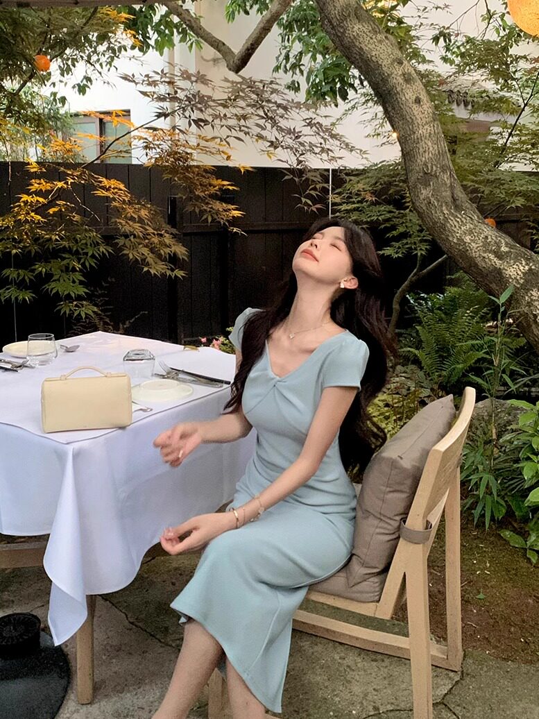 Woman wearing a light blue fitted midi dress outdoors at a garden restaurant