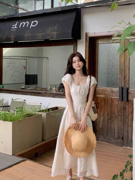 Woman wearing a white flowy puff-sleeve dress holding a straw hat
