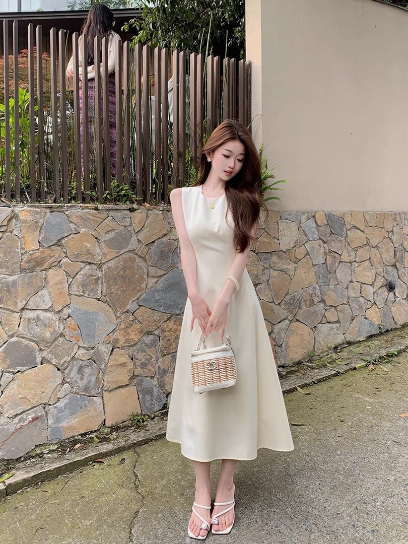 Woman modeling a cream sleeveless midi dress with a small handbag and sandals