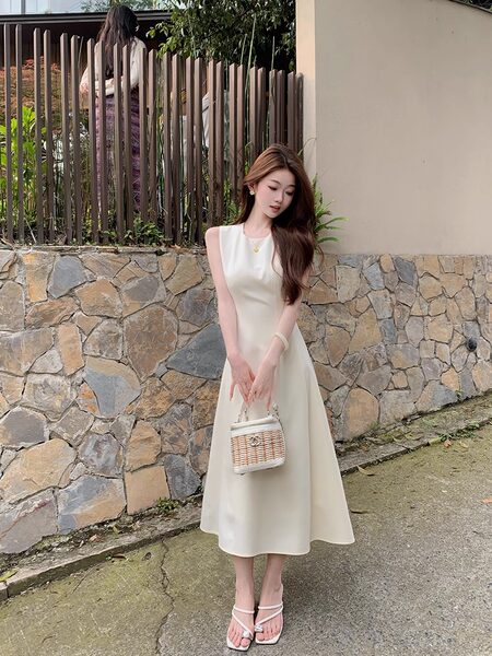 Woman modeling a cream sleeveless midi dress with a small handbag and sandals