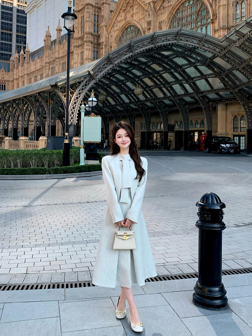 Woman wearing a cream long coat dress and holding a small handbag outdoors