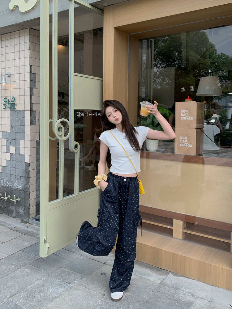 Woman wearing a white fitted crop top and navy polka dot cargo pants outdoors