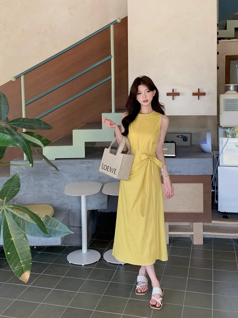 Woman wearing a sleeveless yellow midi dress with a woven tote bag