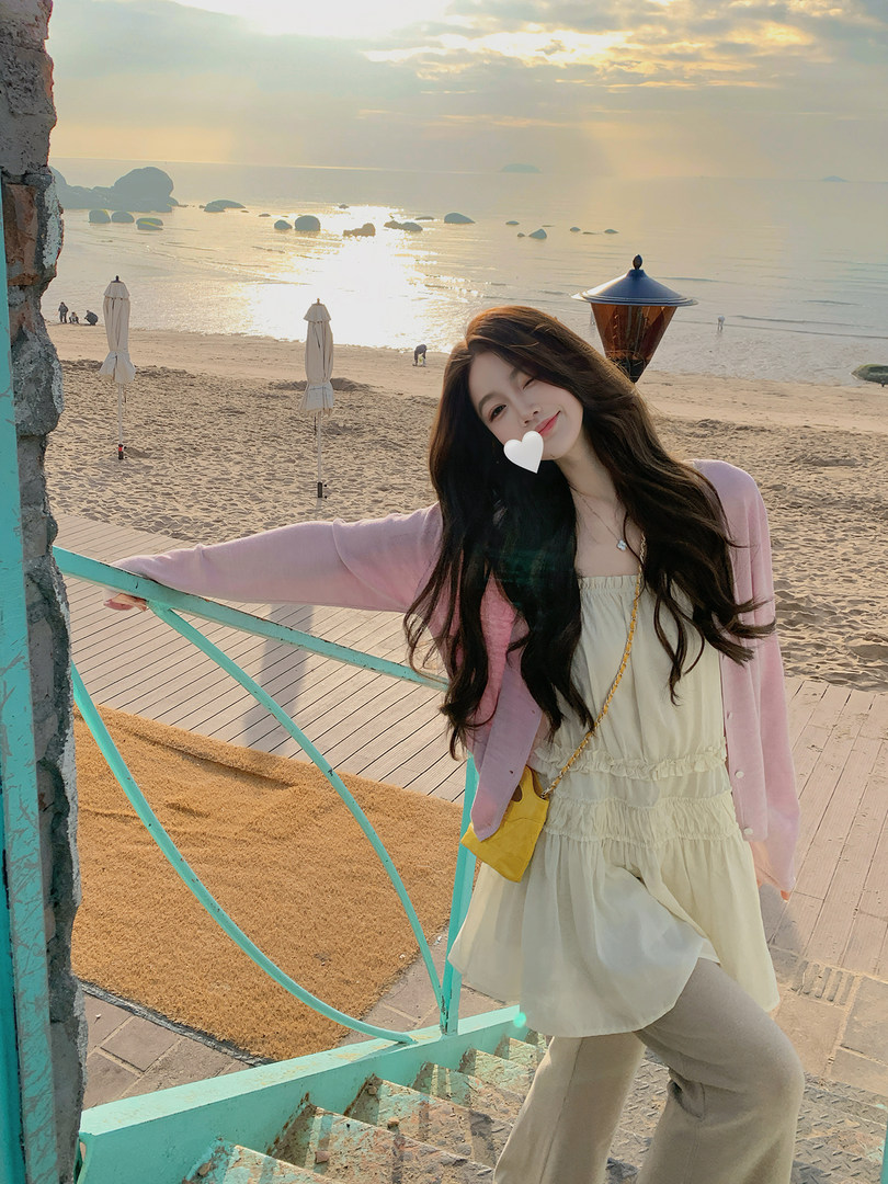 Woman wearing a pink cardigan and cream dress at the beach