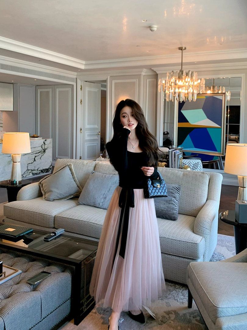 Woman wearing a black top with a pink pleated skirt in a luxury interior