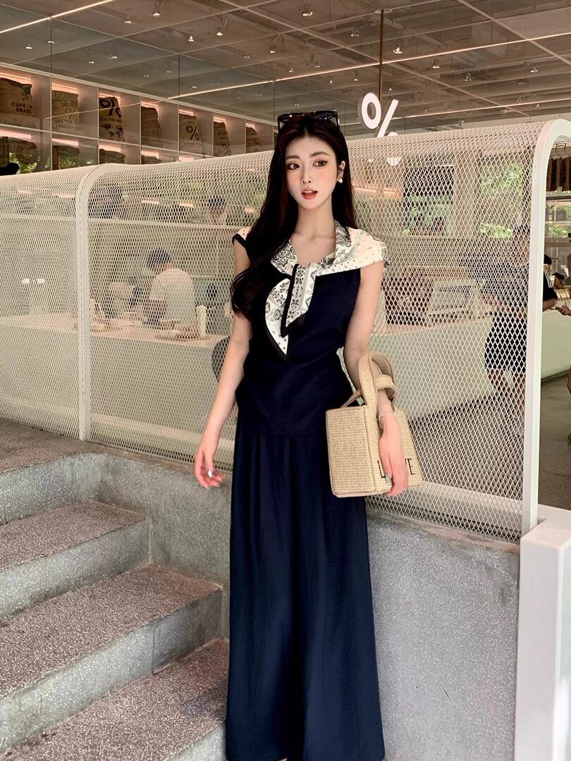 Woman wearing a navy sleeveless long dress with a patterned scarf collar and a woven handbag