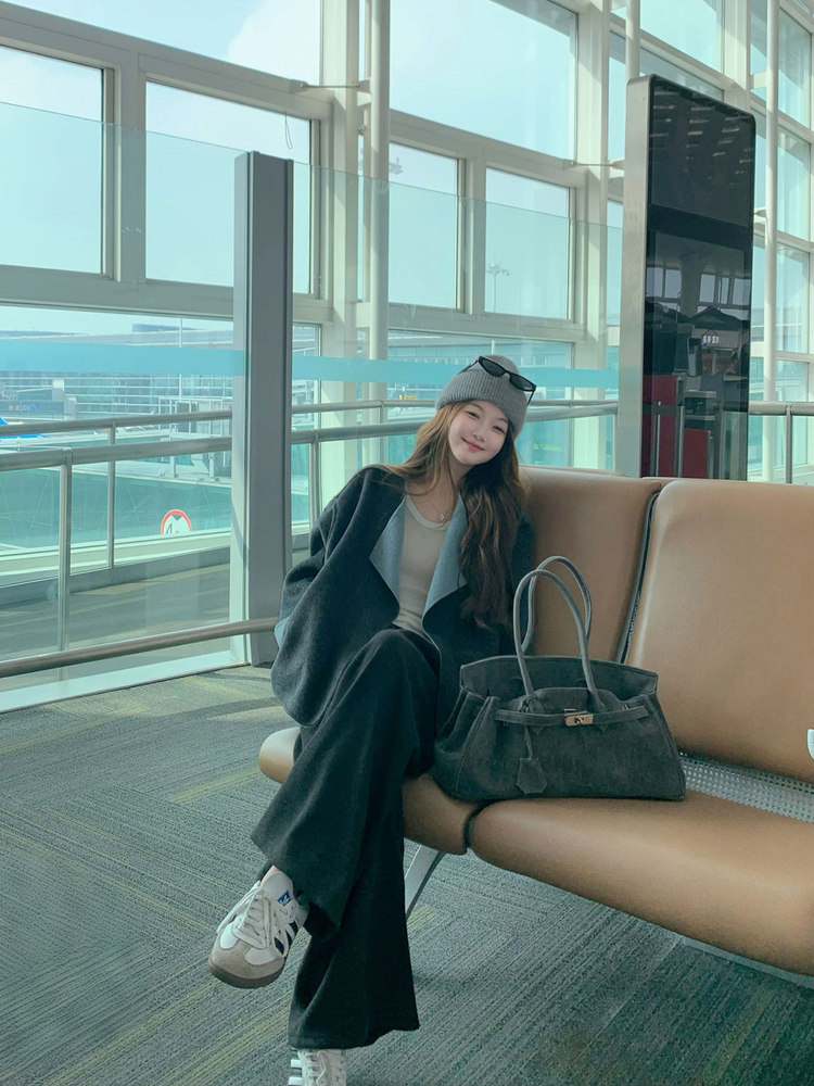 Woman seated in an airport lounge wearing a dark outfit with a black handbag