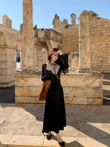 Woman wearing a black long-sleeve maxi dress with a contrasting gray collar and bow detail