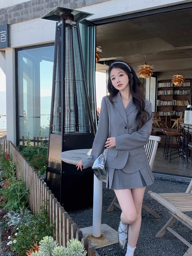 Woman wearing a gray blazer and pleated skirt set with a small silver handbag