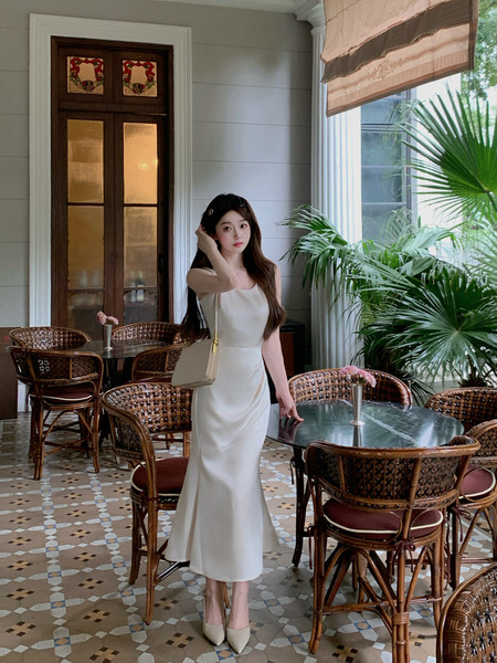 Woman wearing a white elegant sleeveless midi dress with a small handbag