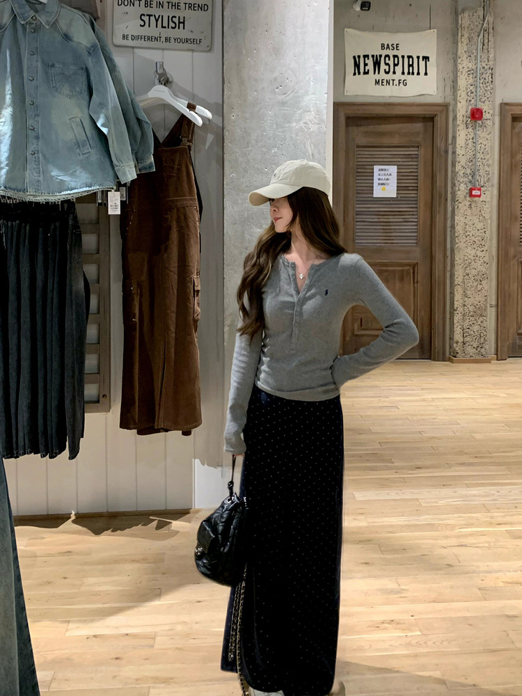 Woman wearing a gray long-sleeve top and black long skirt with a cap and handbag