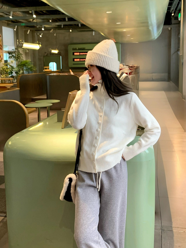 Woman wearing a white knit cardigan and beanie with gray sweatpants and a black shoulder bag