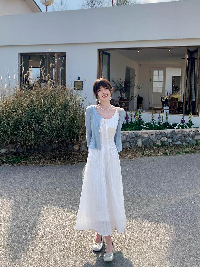 Woman wearing a white midi dress with a light blue cardigan outdoors