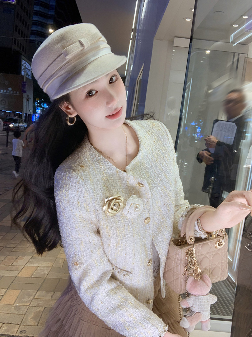 Woman wearing a cream tweed jacket and matching hat while holding a quilted handbag