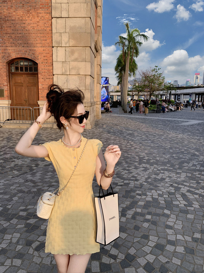 Woman wearing a short yellow dress outdoors with sunglasses and a small white shoulder bag