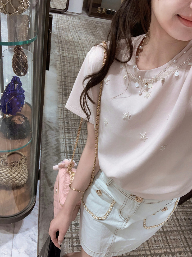 Woman wearing a pastel embellished top and light denim skirt with gold chain details