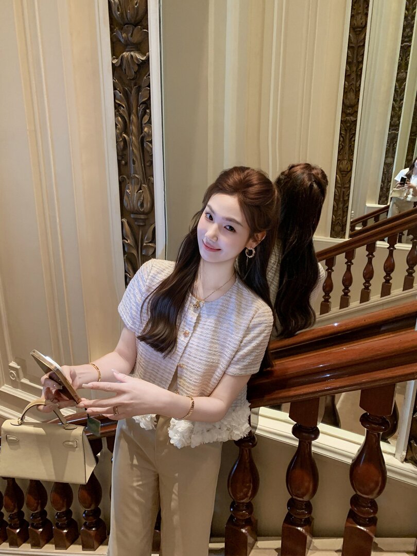 Woman modeling a light short-sleeve top with beige pants and a handbag indoors