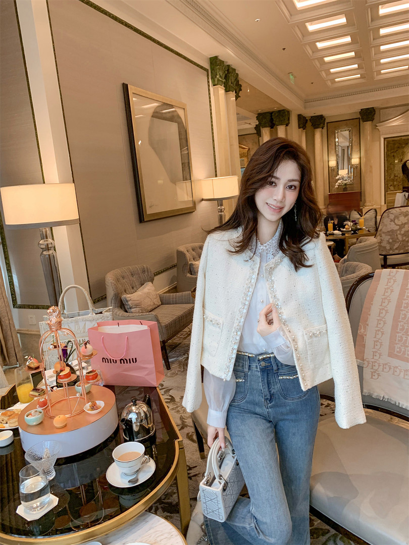 Woman wearing a white embellished cape jacket with blouse and jeans in a luxury lounge setting