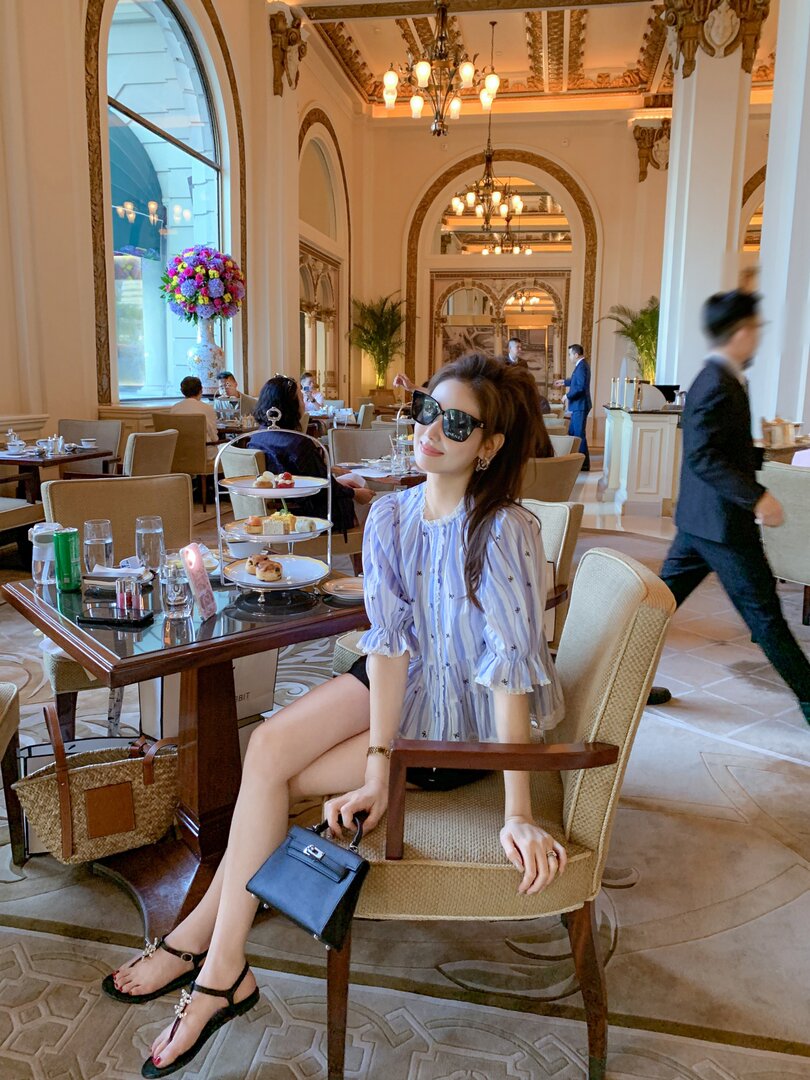 Woman wearing a light blue striped blouse and black sandals seated in an elegant restaurant