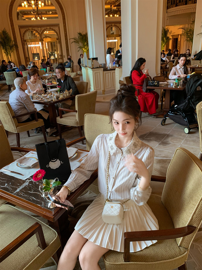 Woman wearing a white pleated dress and carrying a small quilted crossbody bag in a luxury restaurant