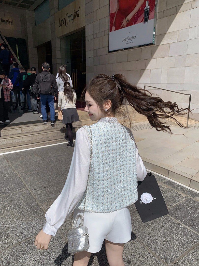 Woman wearing a white outfit with a light blue textured vest and silver mini bag
