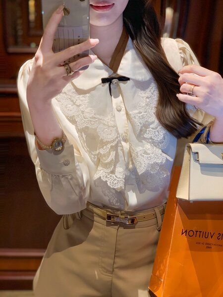 Woman wearing a cream lace-trim blouse with beige trousers and a handbag
