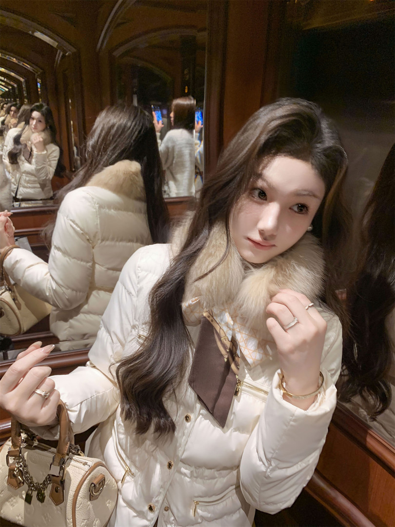 Woman wearing a white puffer jacket with fur collar and gold accents
