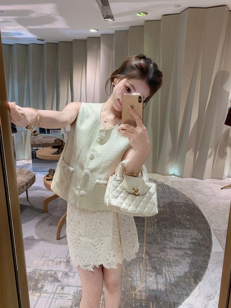Woman wearing a cream sleeveless tweed top and lace skirt holding a quilted white handbag