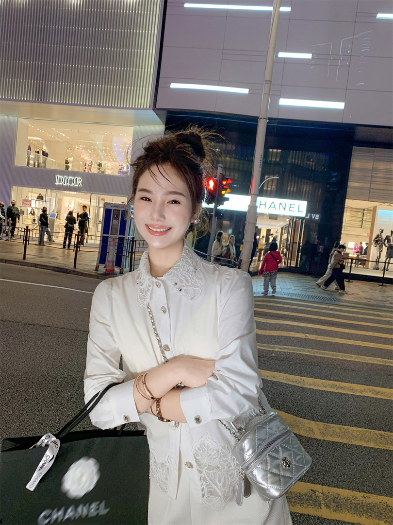 Woman wearing a white embroidered dress with a silver quilted mini handbag outdoors at night.