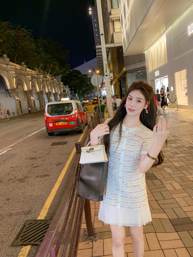 Woman wearing a pastel tweed short-sleeve dress with pleated hem at night on a city street