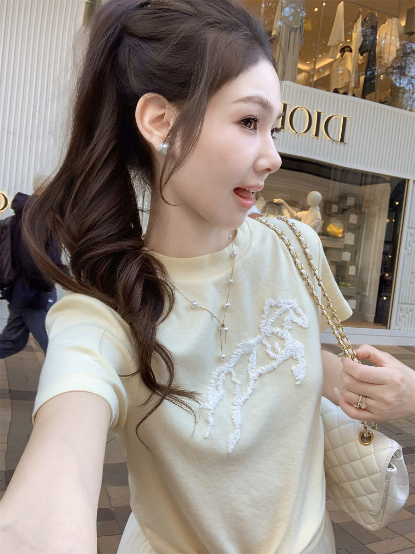 Woman wearing a cream short-sleeve top with a quilted handbag