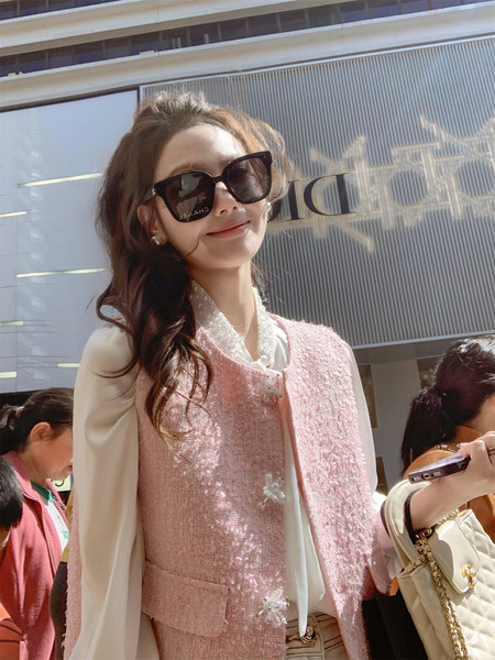 Woman wearing a pink tweed outfit with black cat-eye sunglasses and a white blouse